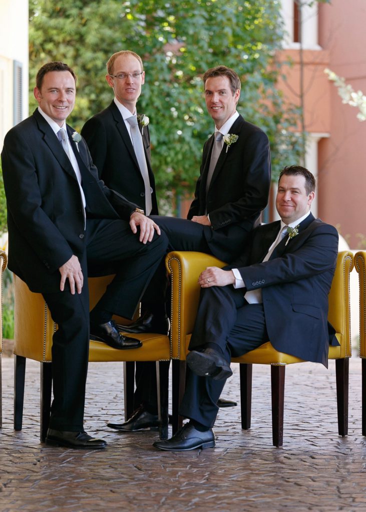 Groomsmen in black suits sitting on yellow chairs at The Wescliff Hotel