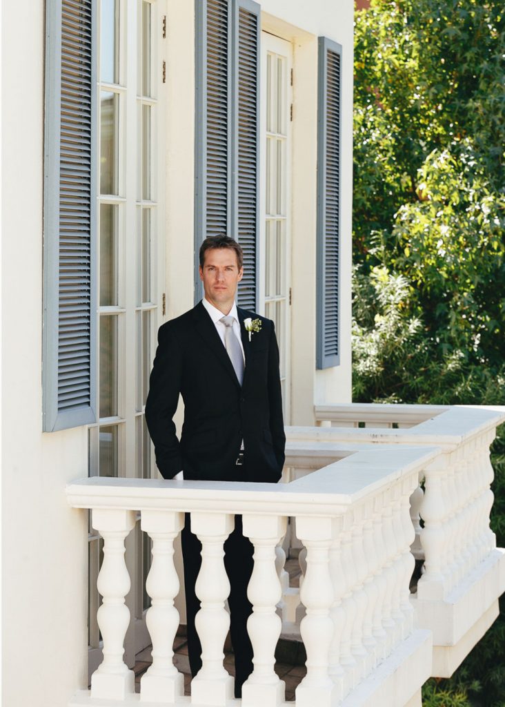 Groom in a black suite with a silver tie standing on the balcony at The Westcliff Hotel