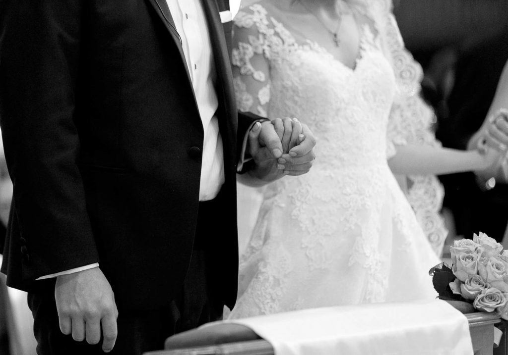 black and white image of bride and groom holding hands in the church at Our Lady Of Cedars on Woodmead