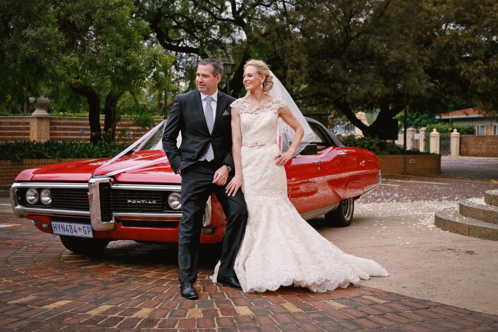 Wedding couple standing in front the red Pontiac wedding carat Die Ooskerk Kirkness Street Clydesdale Pretoria