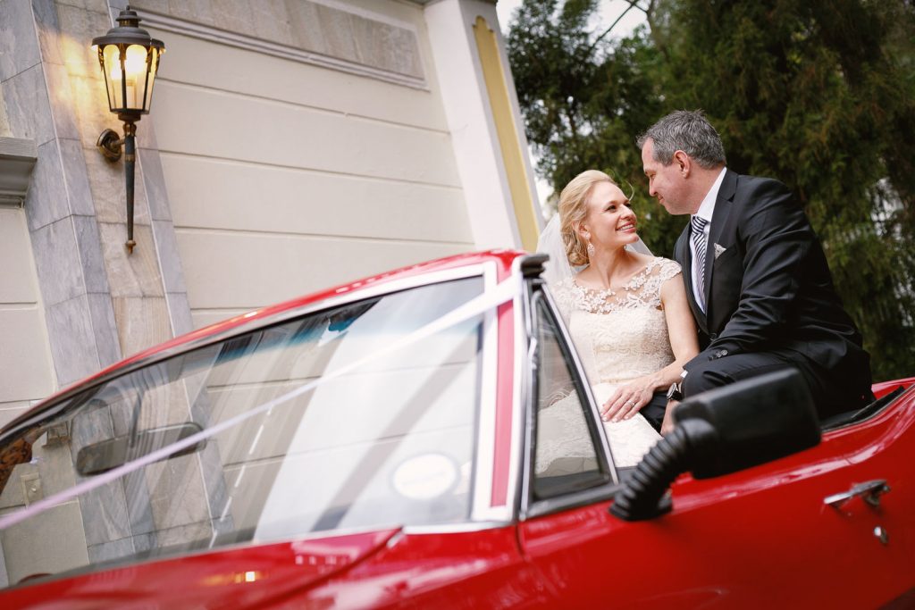 Bride and groom sitting inside their red Pontiac wedding car at Illyria House in Pretoria
