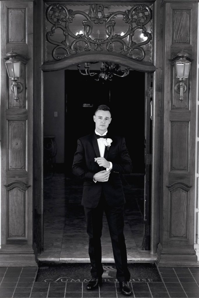 black and white image of groom standing in front of the door at Summer Place Wedding Venue