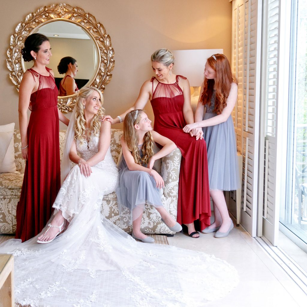 bridesmaids in red and grey dresses sitting on a coach at 12 Apostles Hotel in Cape Town