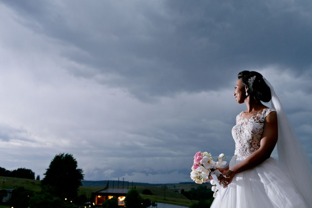 Bride in a white wedding dress overlooking the glass chapel at Brahman Hills at sunset