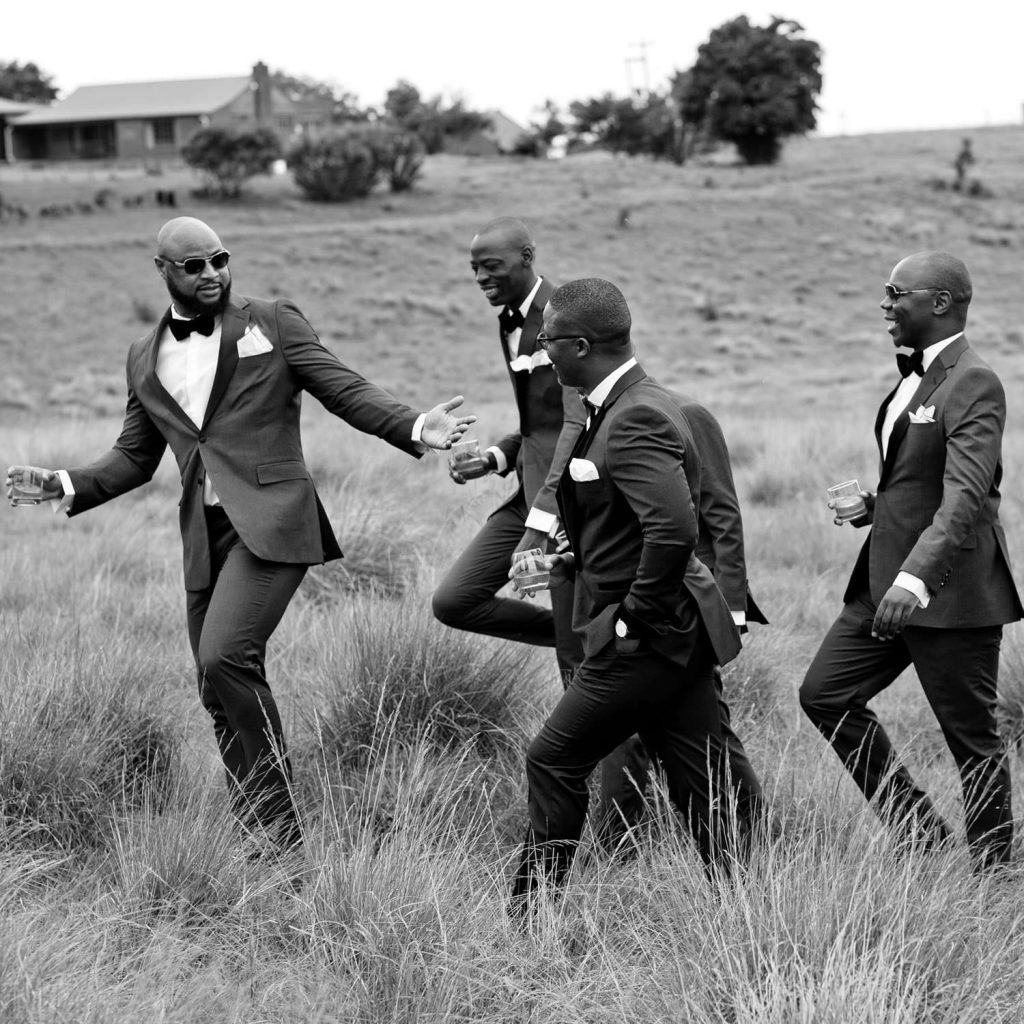 Groomsmen walking through the long green grass at on the hill at Brahman Hills in the Natal Midlands