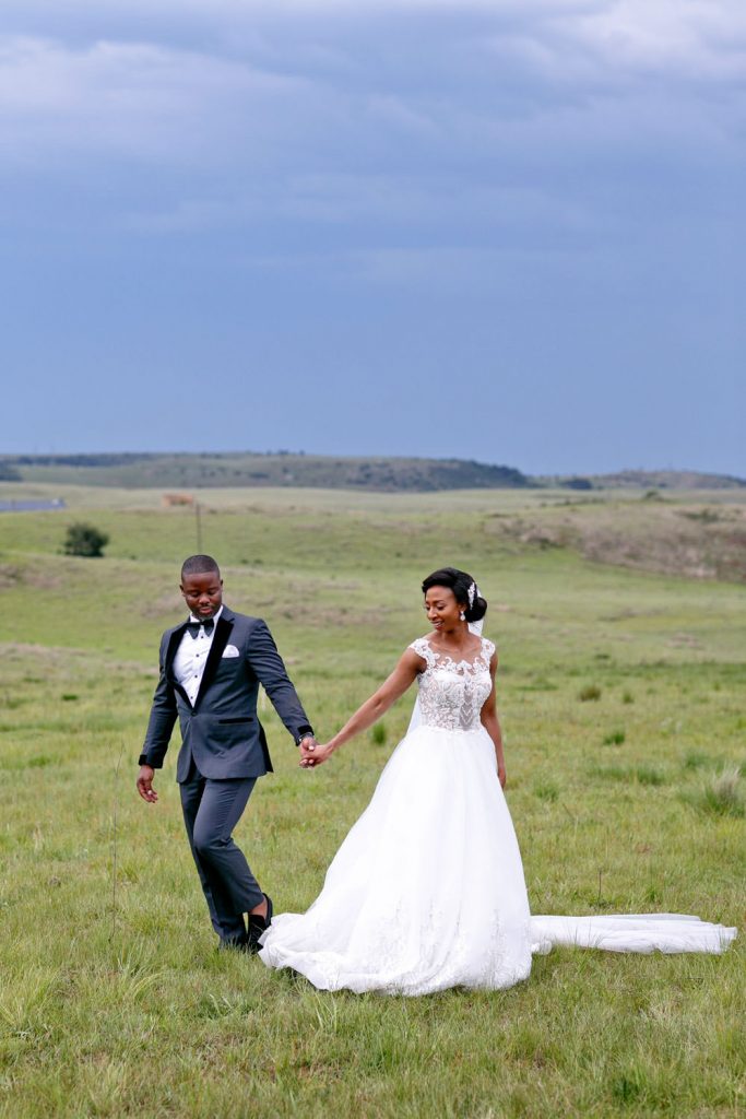 Bride and groom walking in the green grass fields at a wedding venue in Natel