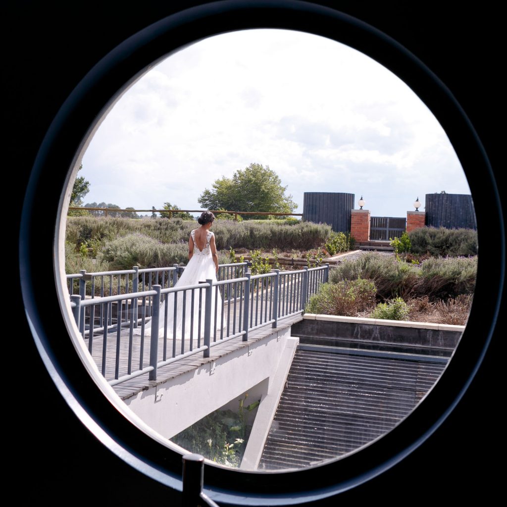 Porthole wedding photograph of the bride walking along the bridge at Brahman Hills Spa