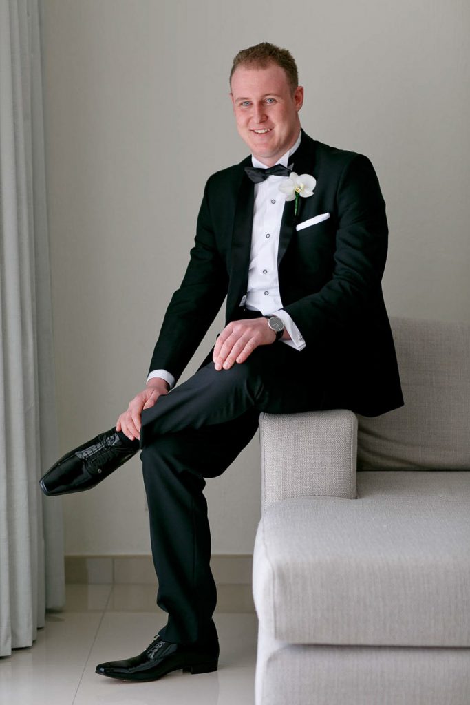Groom in a black suit sitting on a chair at The West Cliff Hotel in Johannesburg