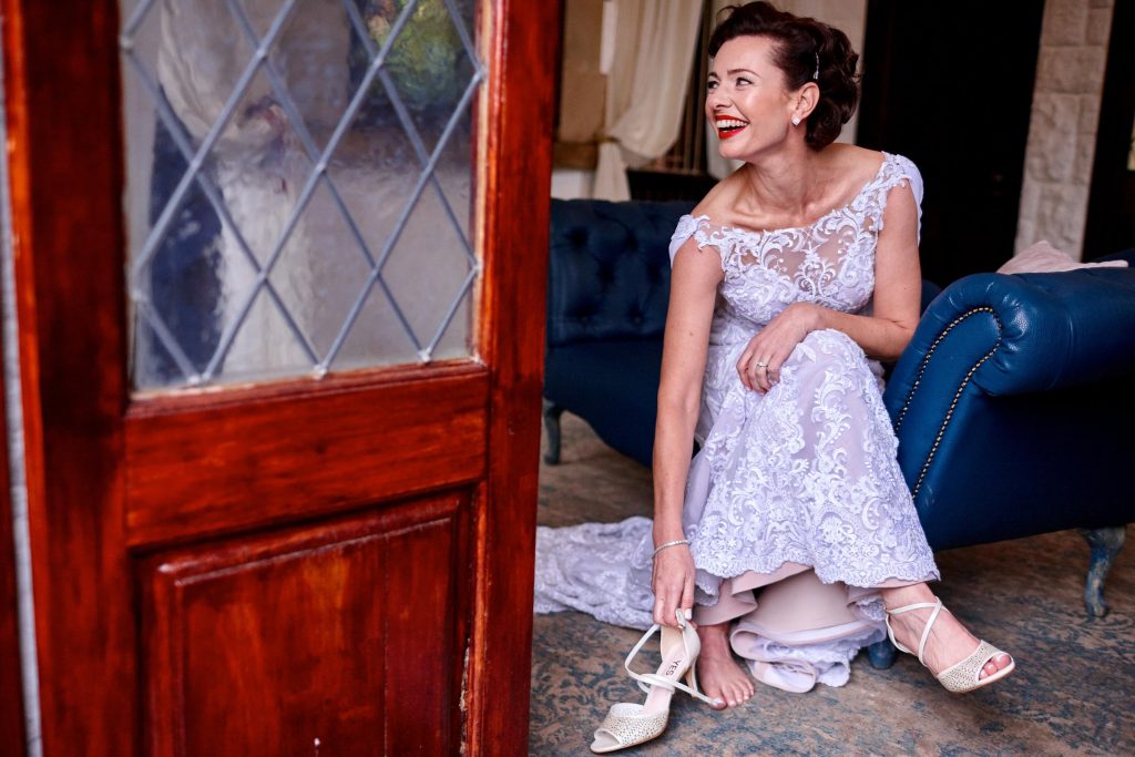 bride in a pink dress slipping on her wedding shoes at Shepstone Gardens