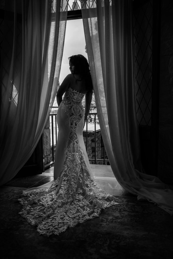 Black and white wedding image of bride standing at the window
